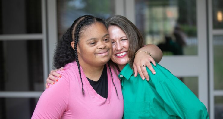 Two women share a warm embrace, one in a pink top and one in a green shirt