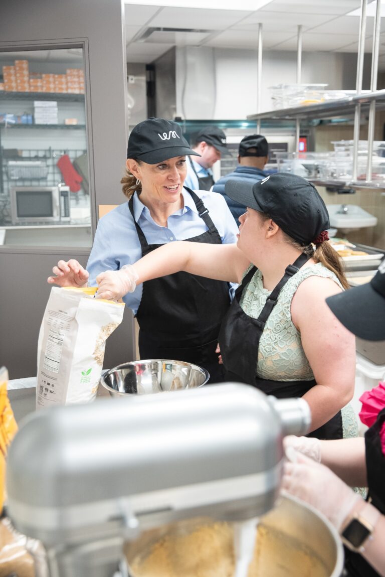 A staff member helps a baker pour flour into a stand mixer