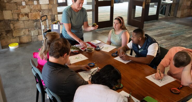 An instructor teaches a group seated at a table in a stone-walled lobby