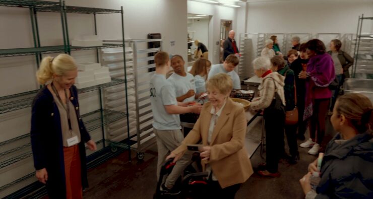Volunteers, staff and guests talking together among speed racks in the Wonderfully Made bakery