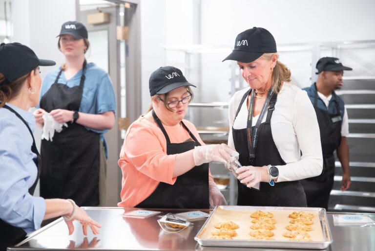 Two bakers decorate cookies together at a stainless prep table