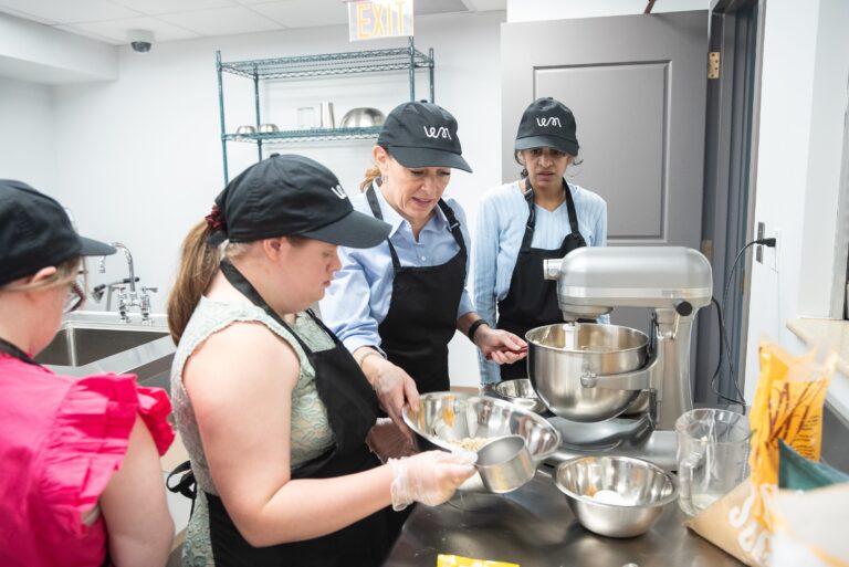 Four bakers gathered around the stand mixer preparing dough
